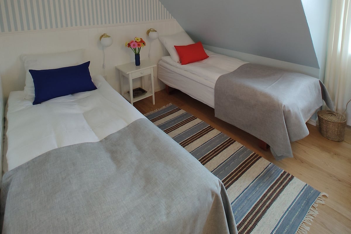 A bedroom with two beds, a nightstand, a lamp, and a small table with flowers.