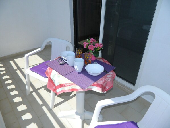 Ein kleiner Tisch im Freien mit einer violetten Tischdecke, weißen Stühlen und einer Blumenschale.