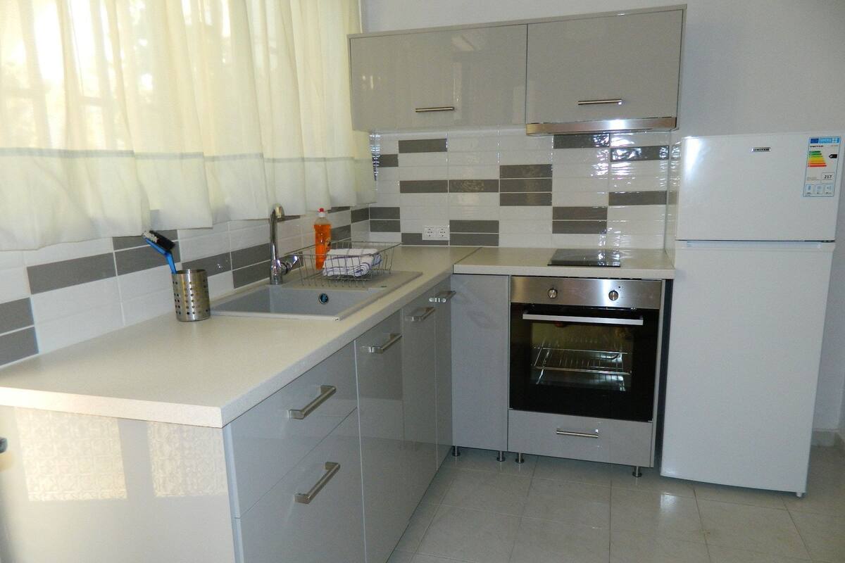 A modern kitchen with a stainless steel refrigerator, oven, and sink. There are white cabinets and a tiled backsplash.