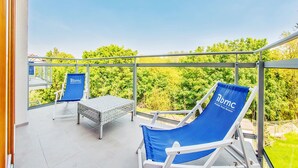 A balcony with two blue lounge chairs and a small table, overlooking a lush green landscape. - Apartments Sopot (Sopot)