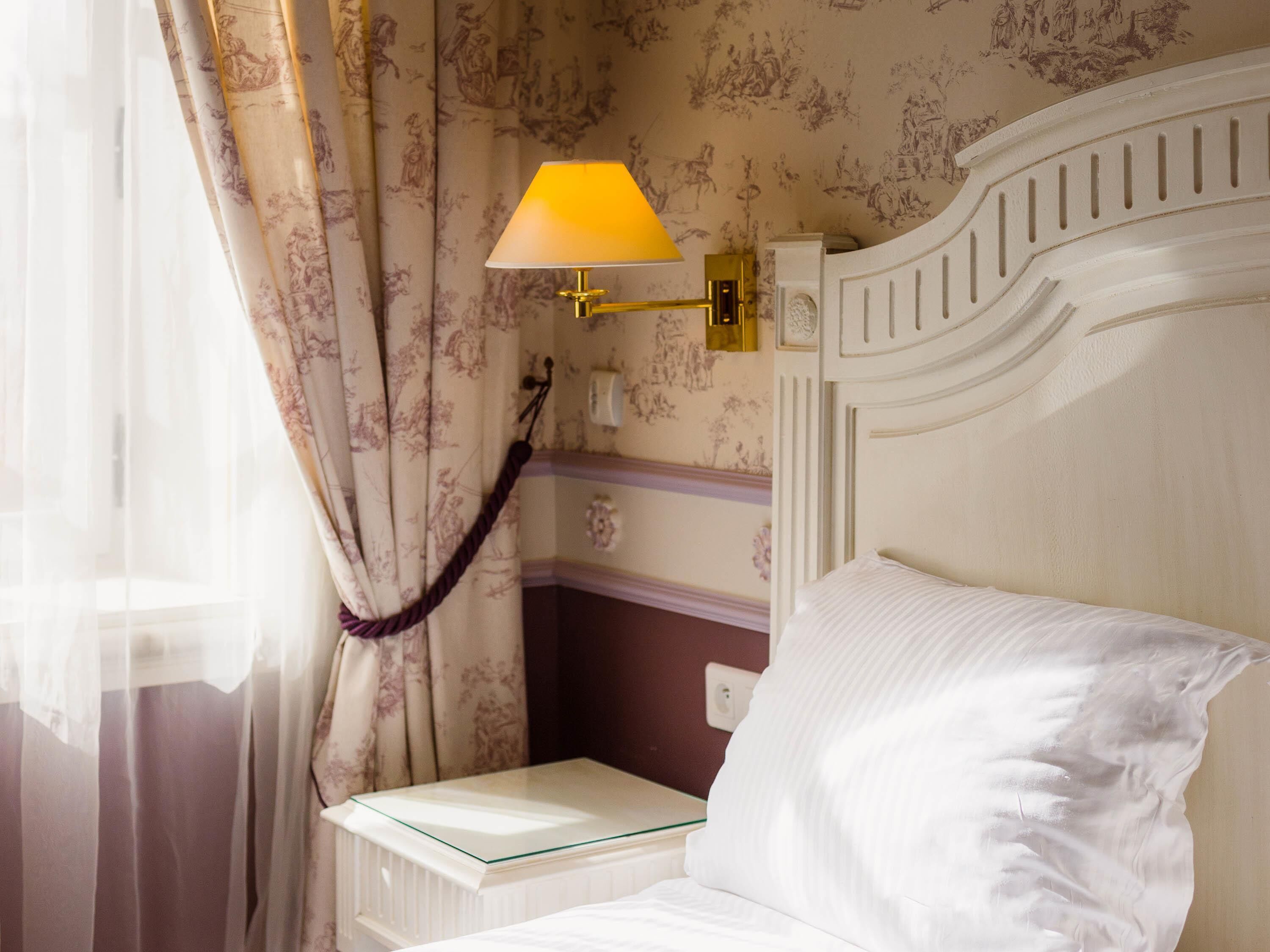 Een hotelkamer met een bed, nachtkastje, lamp en gordijnen.
