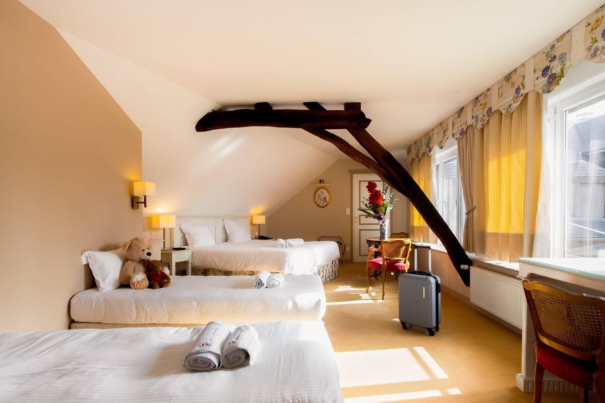 Une chambre d’hôtel avec deux lits, un bureau, une chaise et une fenêtre avec des rideaux.