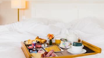 Een ontbijfwagen met gebak, kaas en een kop thee op een bed.