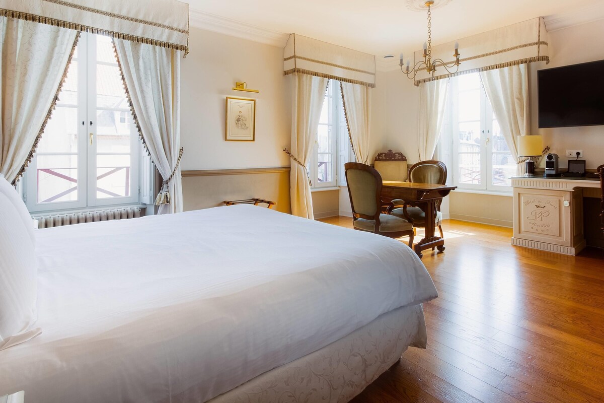A hotel room with a large bed, a desk with a chair, a television, and a chandelier.