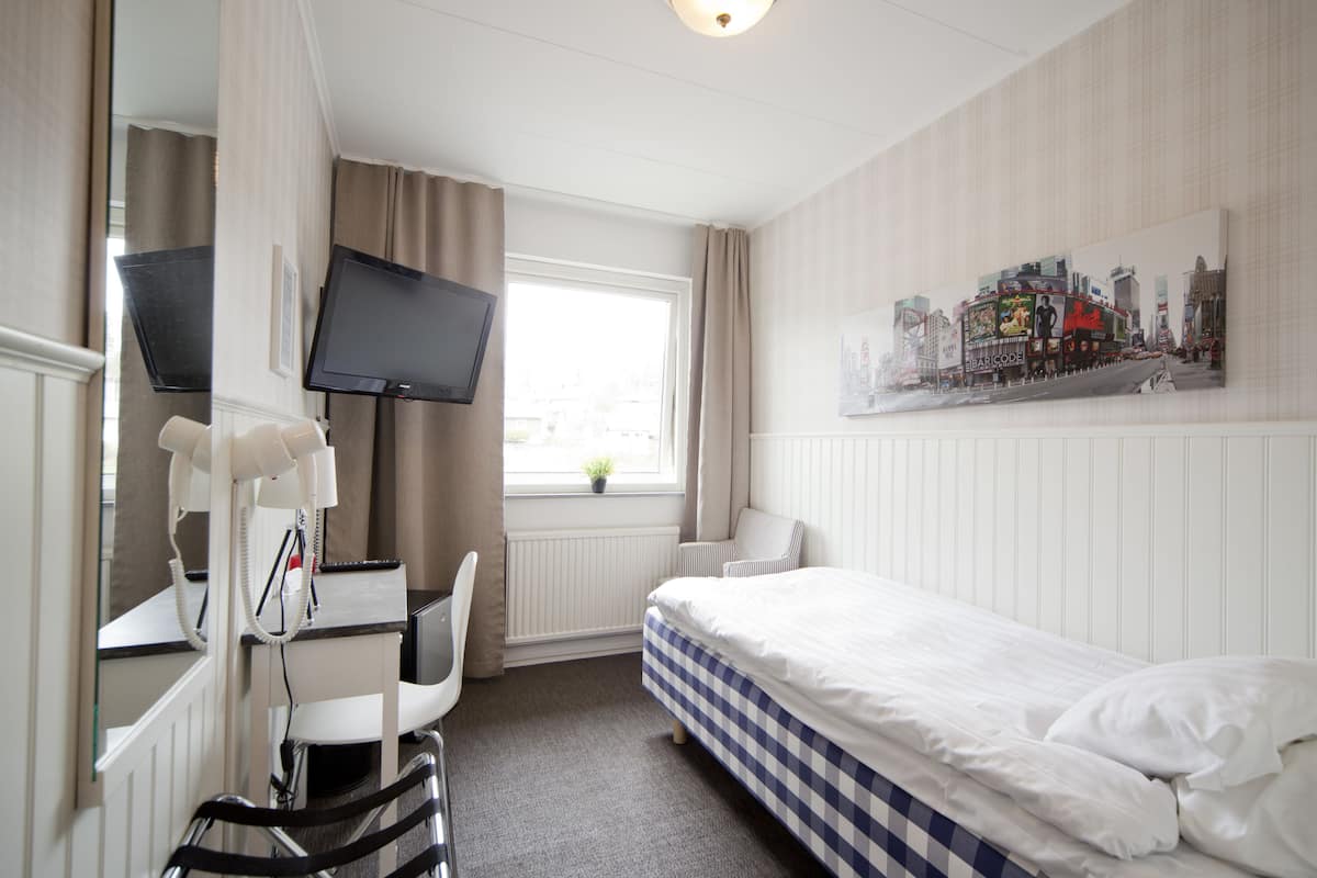 Quarto de hotel com cama, escrivaninha com cadeira, televisão e janela com cortinas.