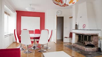 Una sala de estar moderna con una pared de acento roja, un comedor con sillas blancas, una chimenea y un reloj en la pared.