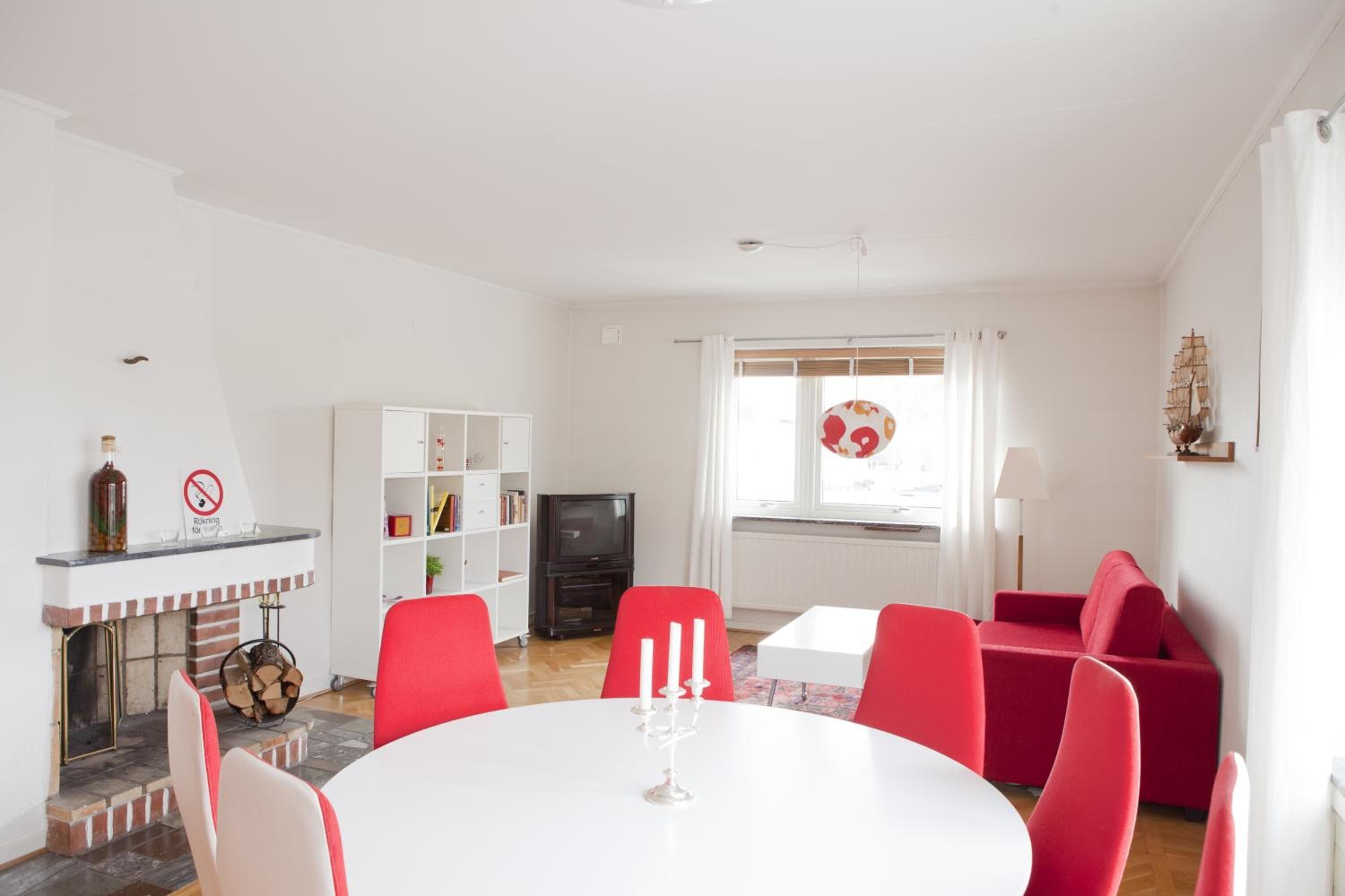 Uma sala de estar moderna com lareira, poltronas vermelhas, uma mesa branca e uma televisão.