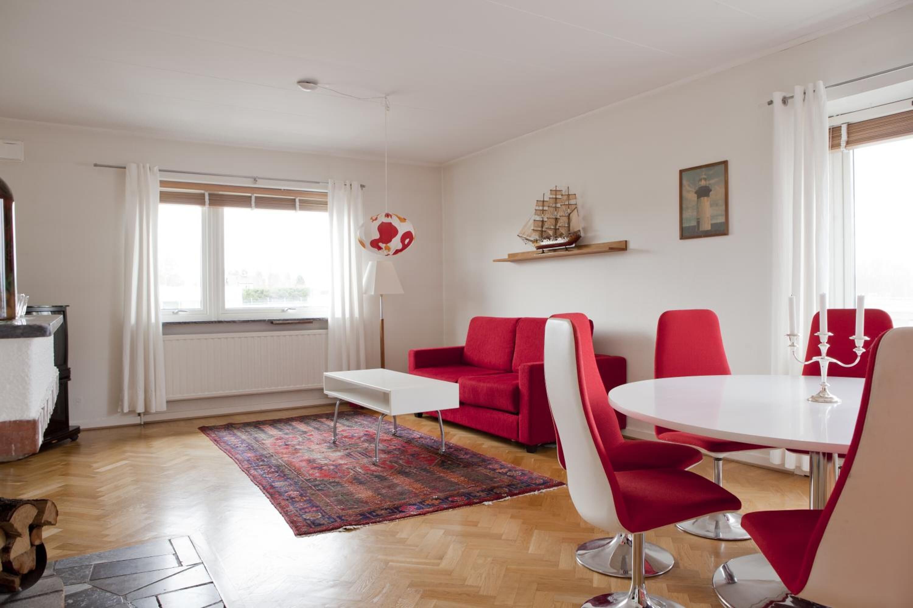 A modern living room with a red sofa, white coffee table, and red chairs around a white dining table.