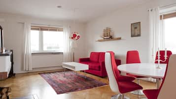 A modern living room with a red sofa, white coffee table, and red chairs around a white dining table.
