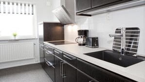 A modern kitchen with dark cabinetry, a white countertop, a coffee maker, and a sink with a towel rack. - Lages Motel & Restaurang (Bramhult)