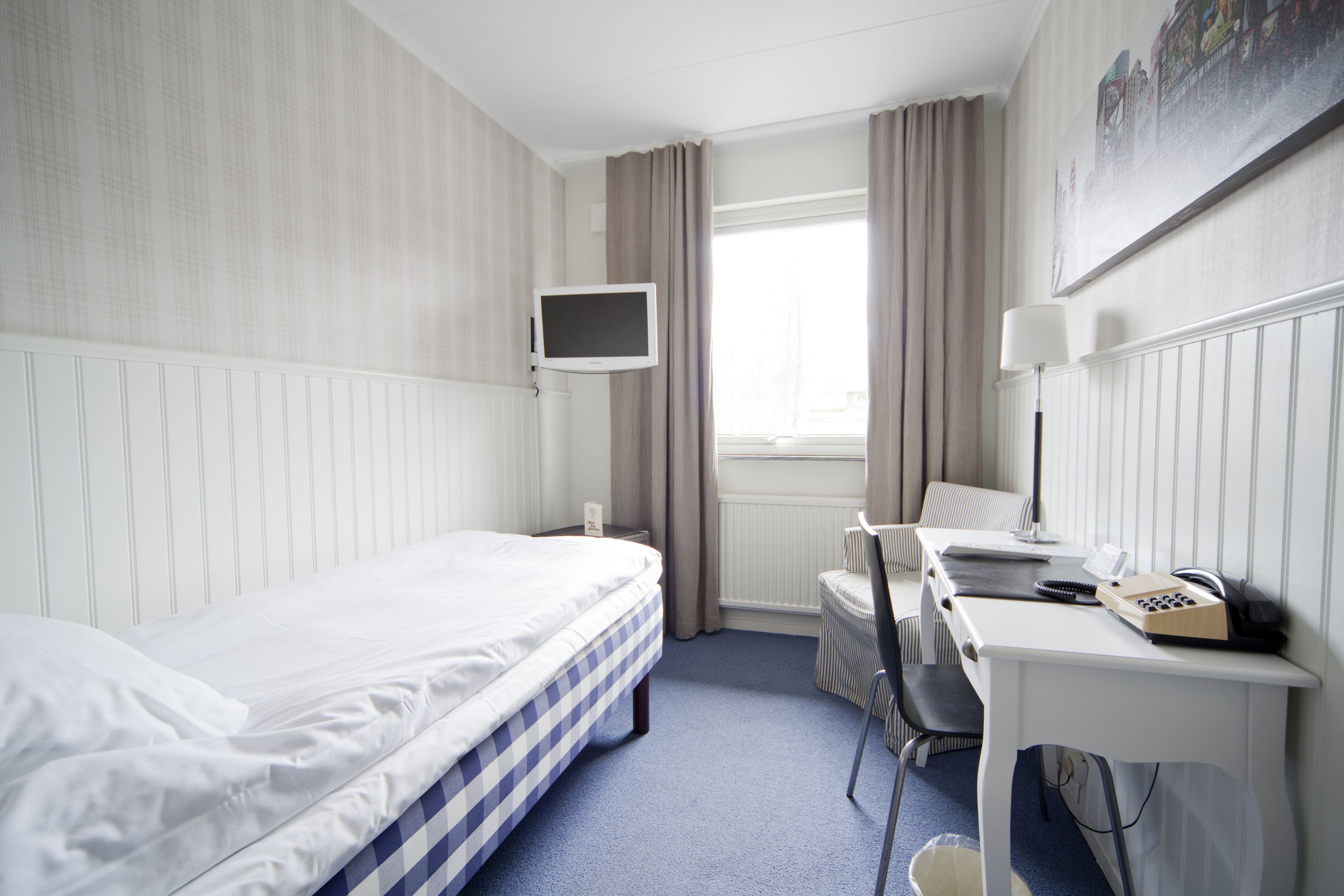 A hotel room with a bed, desk, chair, and a television.