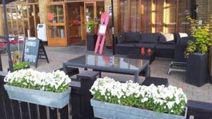 An outdoor seating area with a glass table, black outdoor furniture, and planters with white flowers. - Lages Motel & Restaurang (Bramhult)