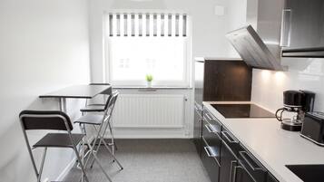 Una cocina moderna con encimera blanca, electrodomésticos de acero inoxidable y una ventana con persianas.