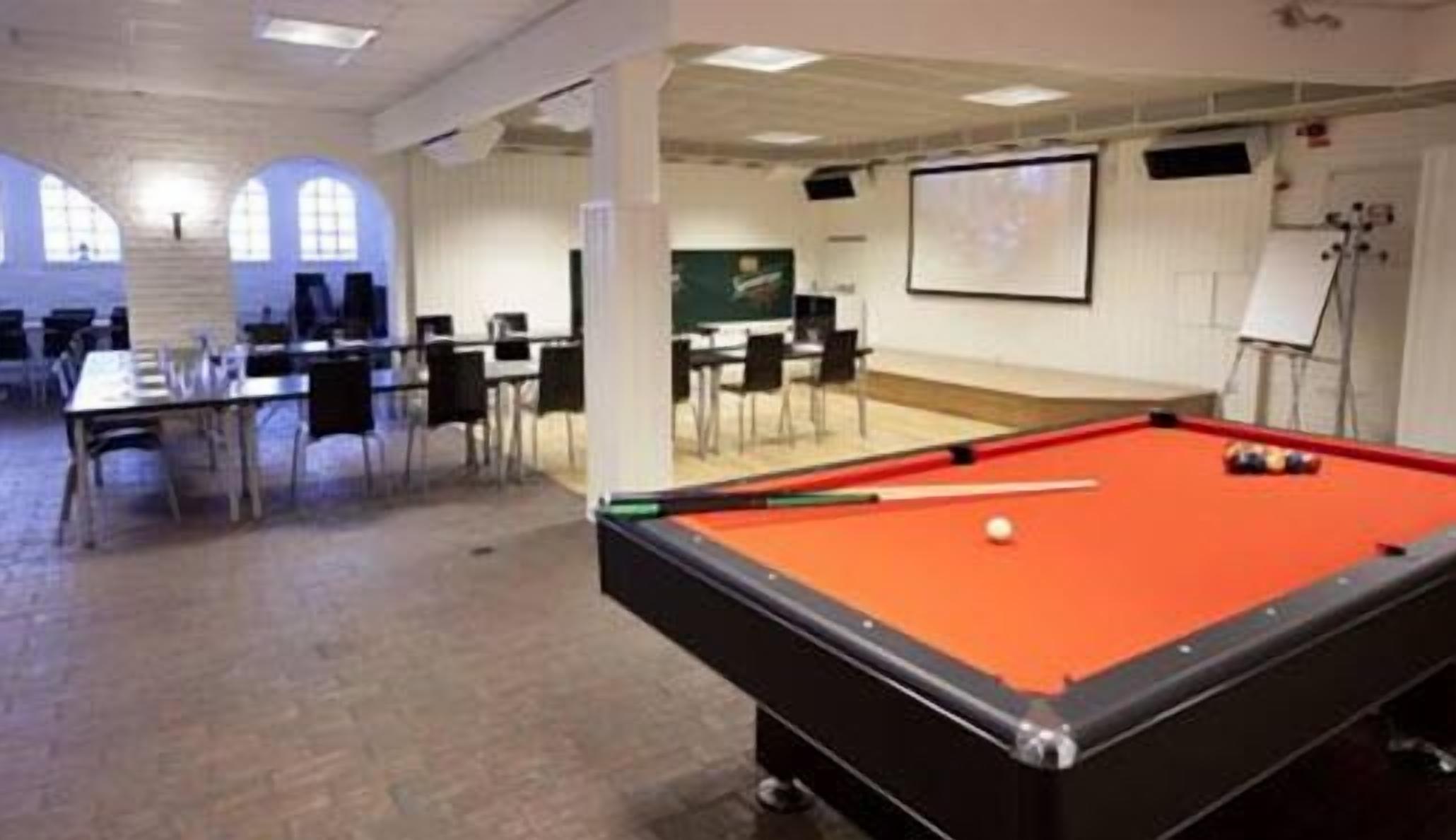 Una sala de billar con mesa de pool, sillas y pantalla de proyector.