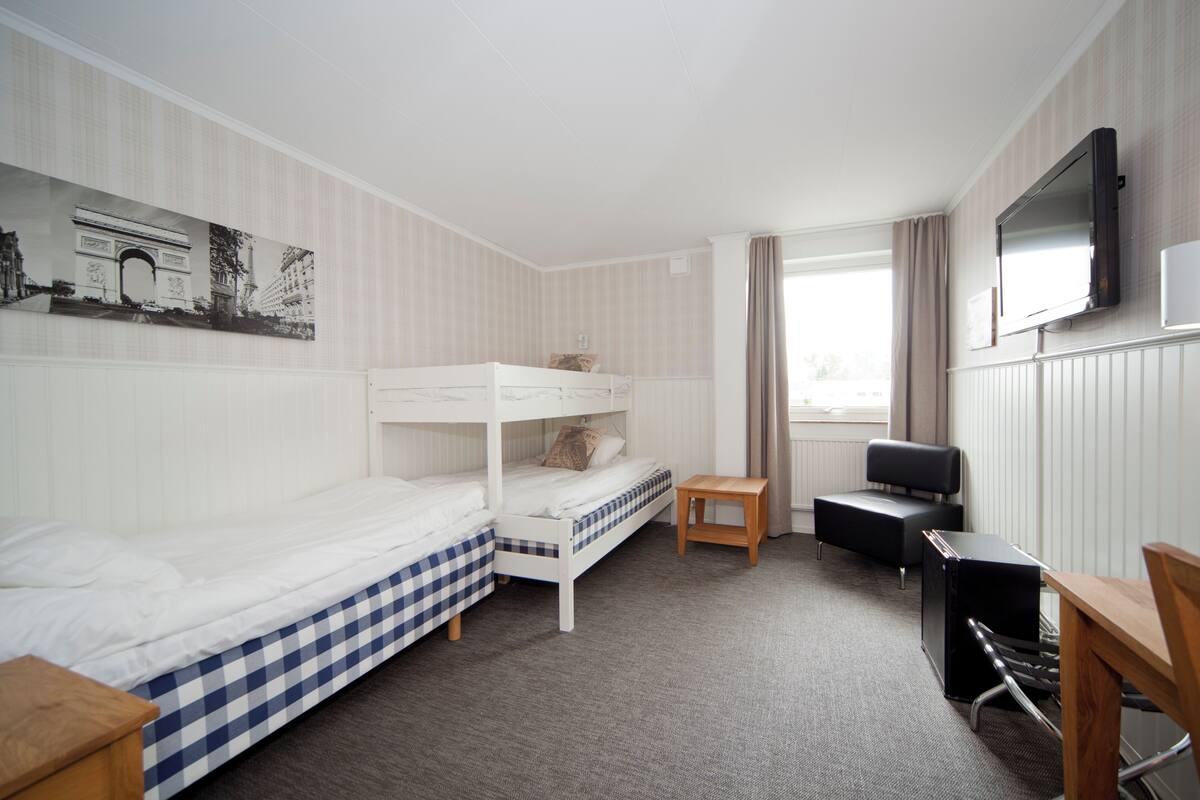 Quarto de hotel com duas camas, uma escrivaninha, televisão e uma janela com cortinas.