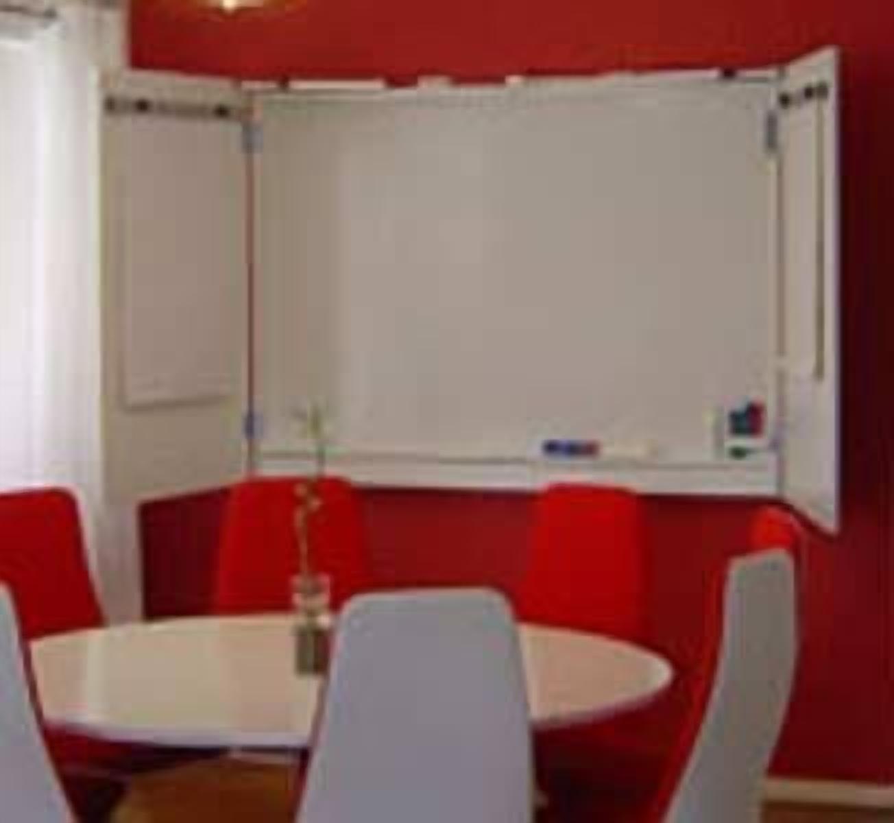 A conference room with a white table and red chairs, a whiteboard, and a small plant on the table.