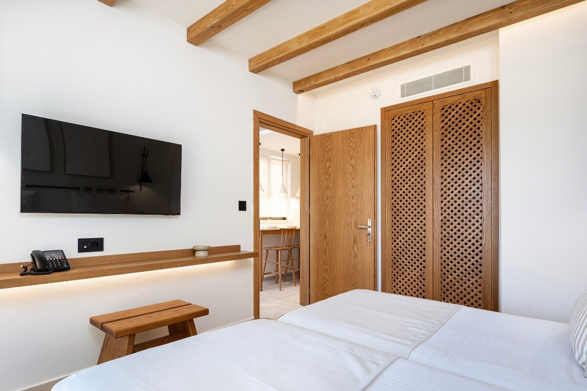 A bedroom with a bed, a bedside table with a phone, a TV mounted on the wall, and a wooden wardrobe.