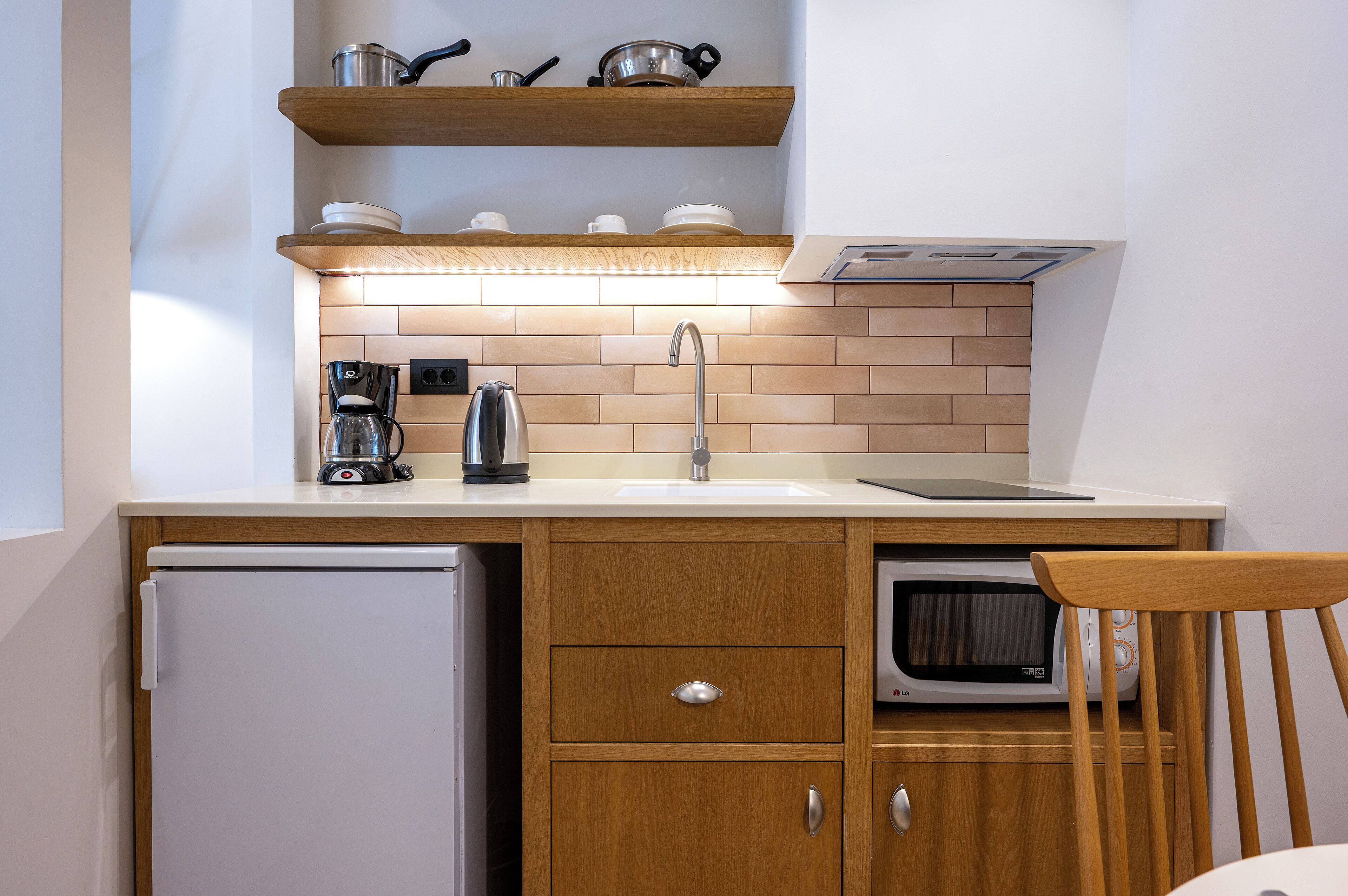 A compact kitchen with a refrigerator, microwave, coffee maker, and wooden cabinets.