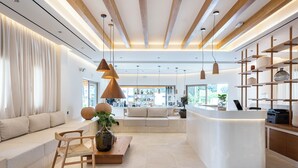 Un interior moderno con un mostrador de recepción curvo, un área de descanso con sofá y sillones, iluminación colgante y un ventanal que proporciona luz natural.