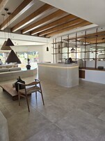 Un interior espacioso y moderno con una isla central, vigas de madera en el techo y un gran ventanal que ofrece vistas al exterior.