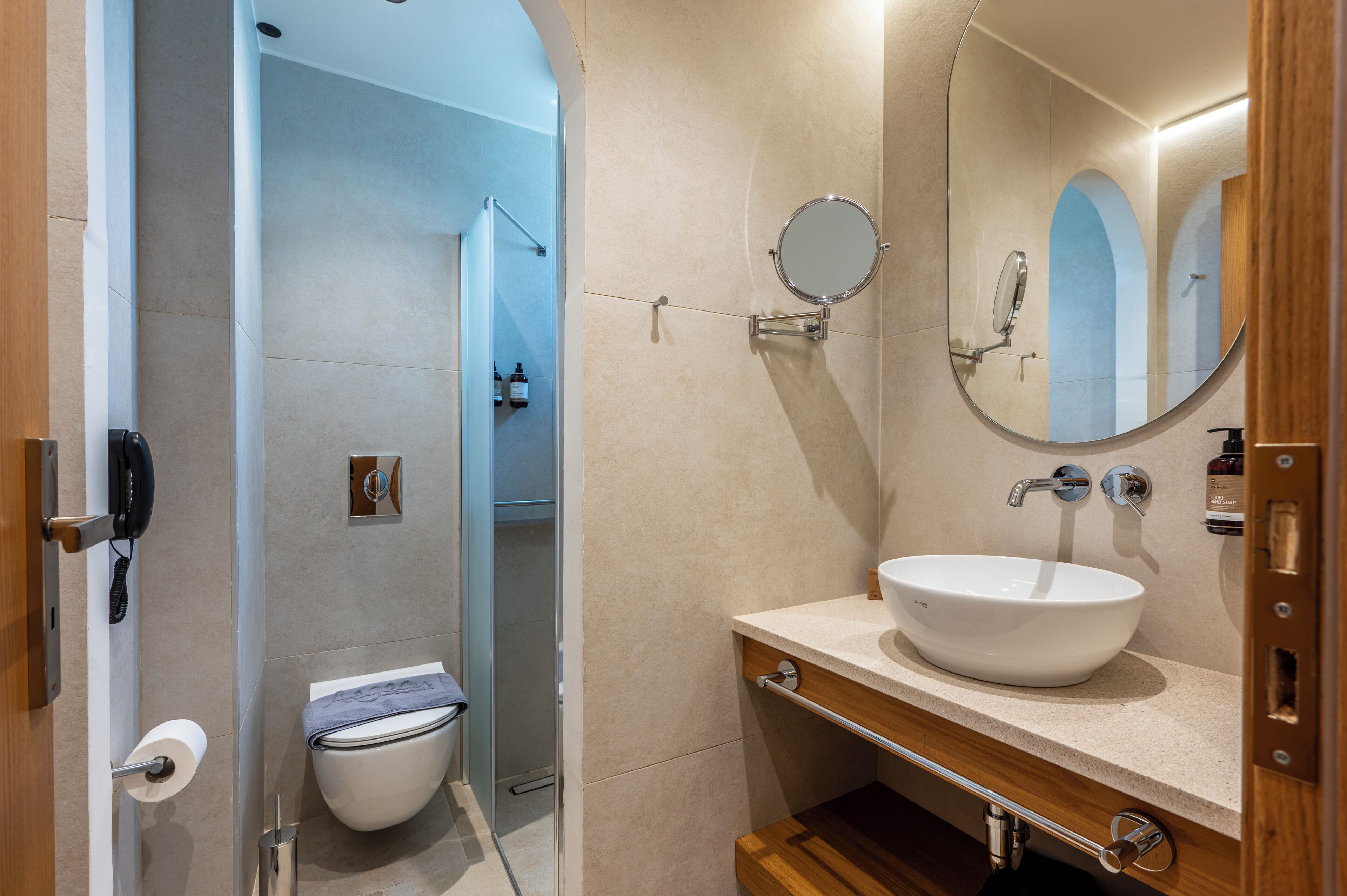 A modern bathroom with a white sink, a round mirror, and a toilet.