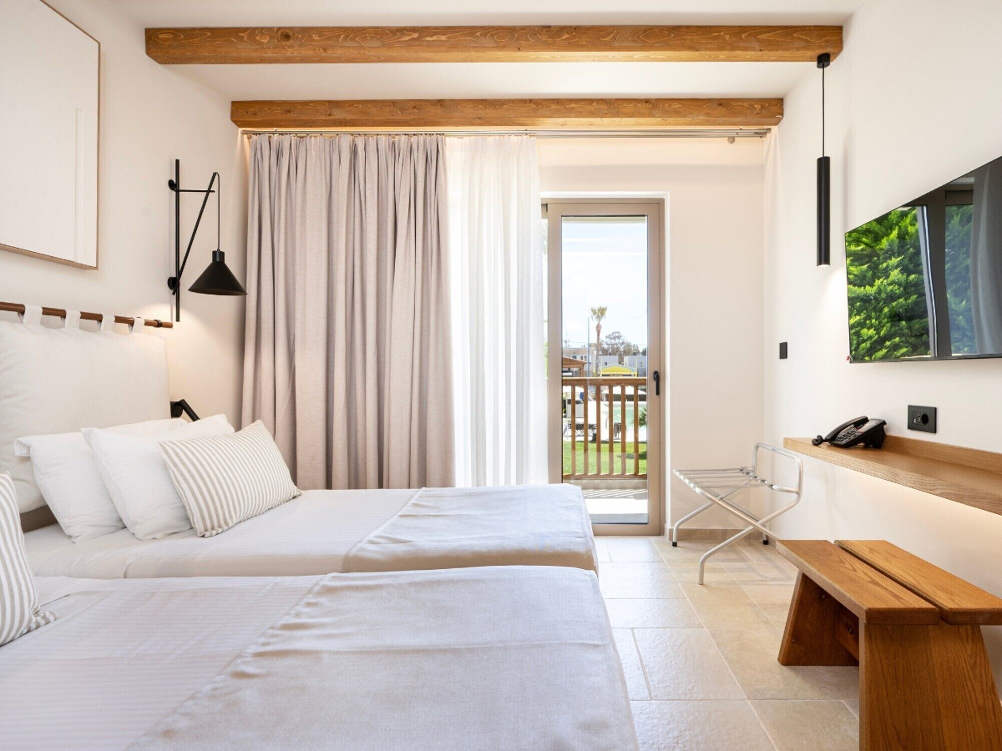 A hotel room with two beds, a balcony, a TV, and a desk with a phone.