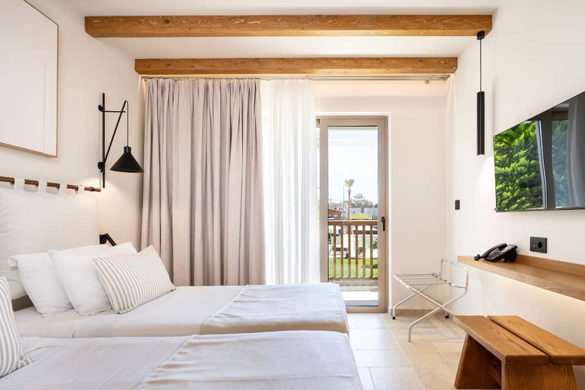 Quarto de hotel com duas camas, uma varanda, televisão e uma secretária com telefone.