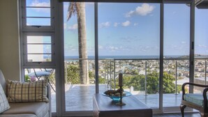 A balcony with a view of the city and ocean. There is a sofa, a coffee table, and a chair. - The Lookout Guest House (Port Alfred)