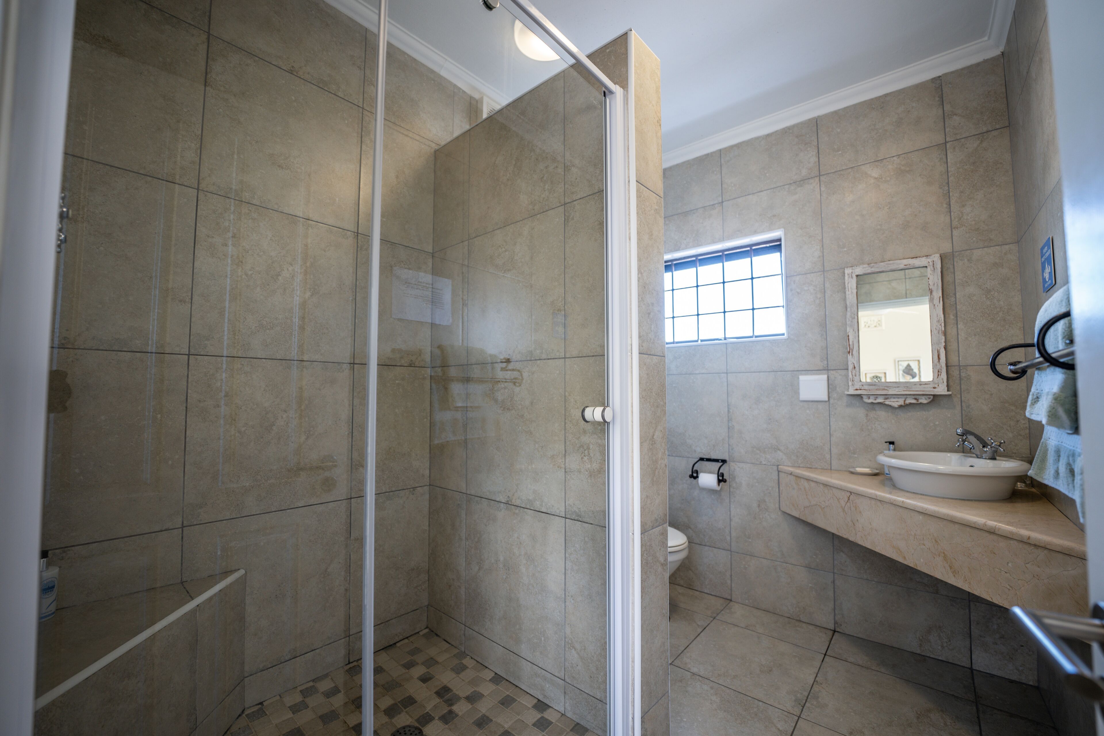 A bathroom with a glass shower enclosure, a toilet, and a sink with a mirror above it.