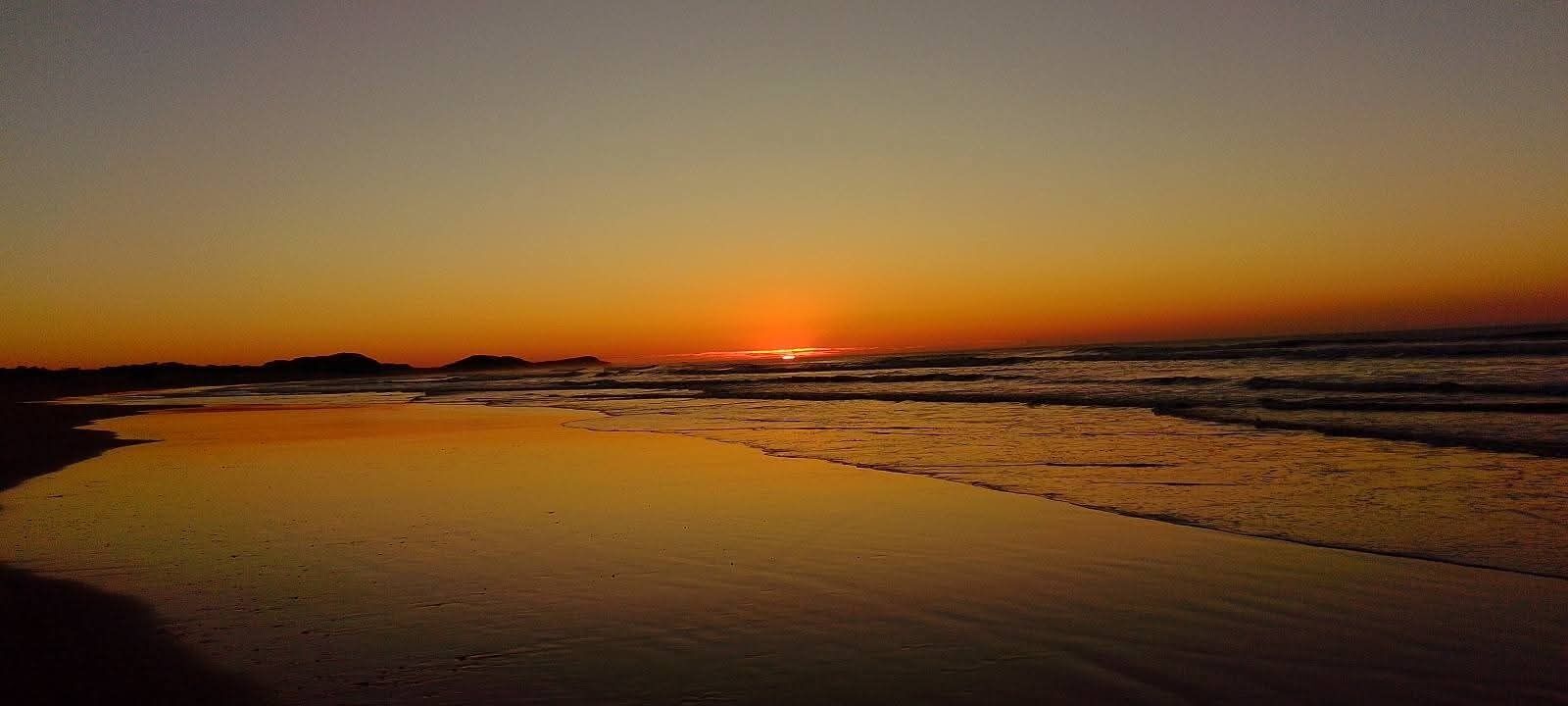 Escena de playa con un atardecer, agua tranquila y una orilla arenosa.