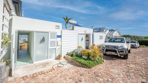 A white building with a garage door, a paved driveway, and a parked truck. - The Lookout Guest House (Port Alfred)