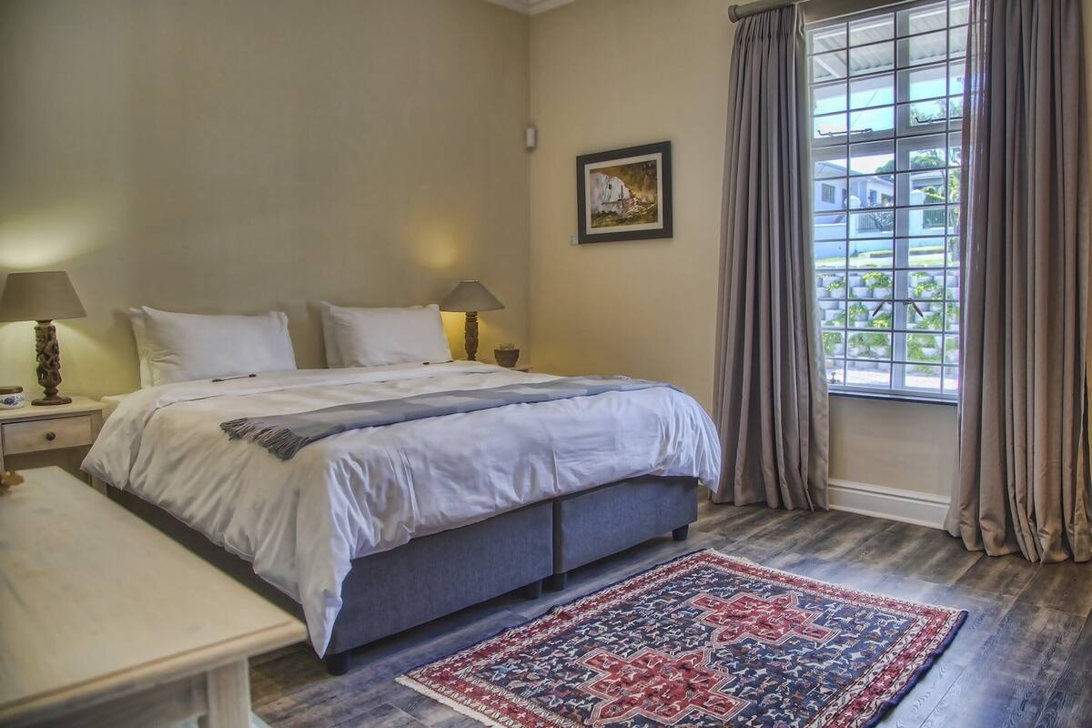A bedroom with a bed, bedside tables, a bench, a window with curtains, and a rug.