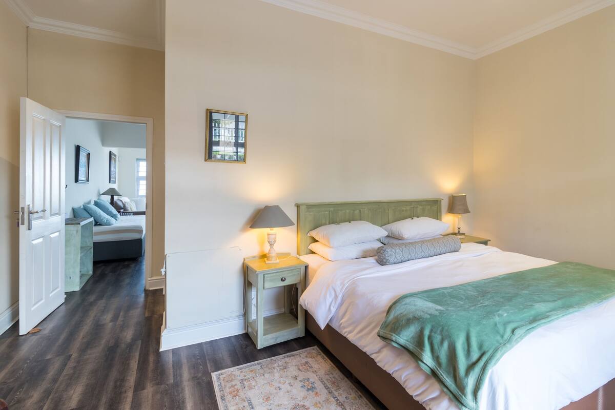 A bedroom with a bed, bedside tables, a nightstand, a mirror, and a door leading to another room.