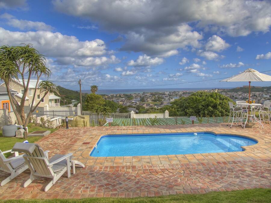 Un patio trasero con piscina, muebles de jardín y vista a una zona residencial.