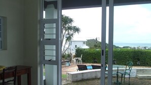 A room with a sliding glass door leading to a patio with a pool, outdoor furniture, and a view of the ocean. - The Lookout Guest House (Port Alfred)