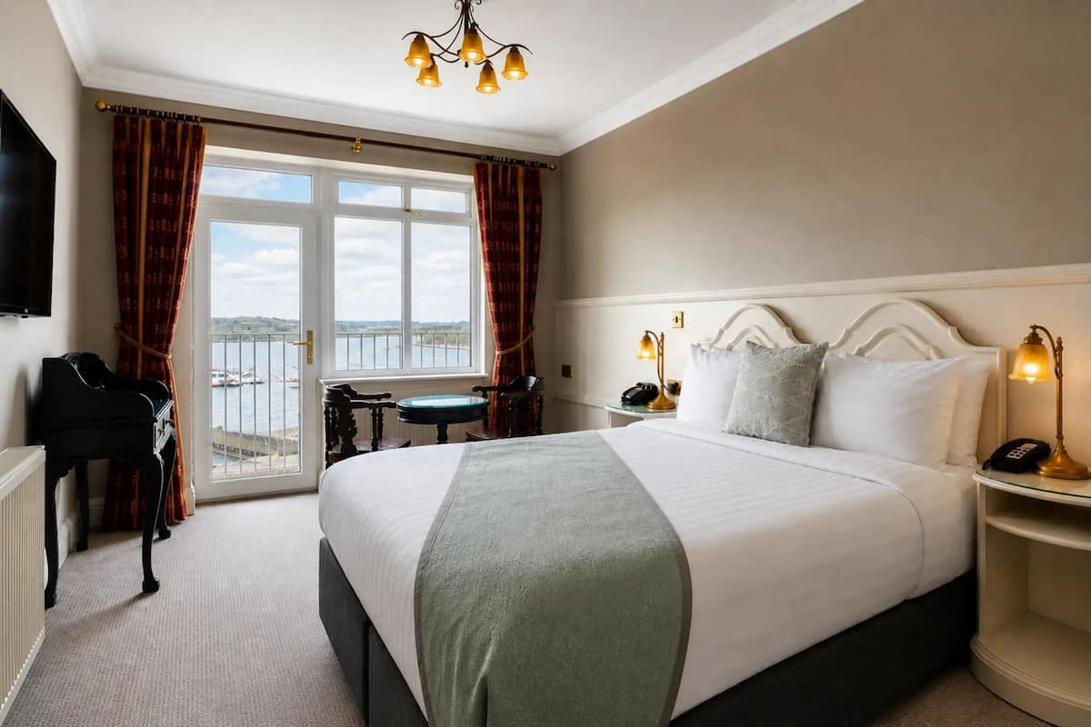 A hotel room with a bed, a desk, a piano, and a view of the sea.