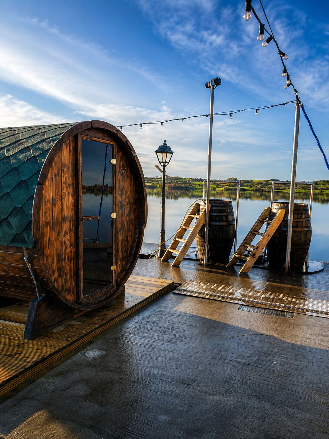 A wooden barrel room with a ladder and barrels, a wooden door, and a view of a lake.