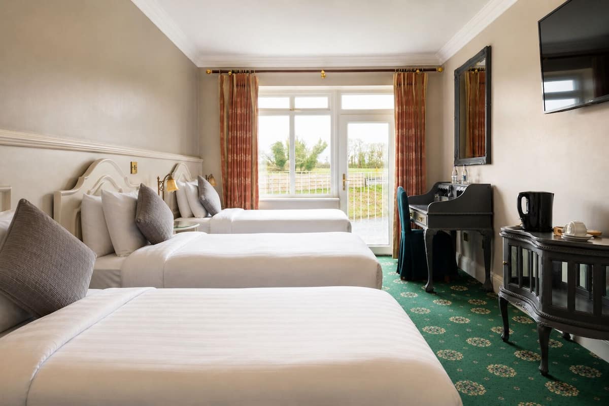 A hotel room with two beds, a desk, a television, and a view of the outdoors.
