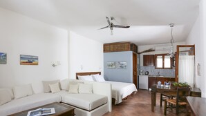 Una habitación de hotel con sofá, dos camas, una mesa de comedor y zona de cocina.