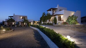 Una villa moderna con camino pavimentado, jardín ajardinado y varias construcciones con iluminación exterior.
