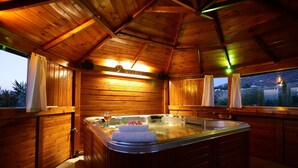 Interior de una cabaña de madera con jacuzzi, paredes de madera y vistas a través del ventanal.