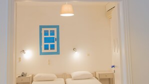 Una habitación con dos camas individuales, una mesita de noche pequeña con lámpara, una luz de pared y una lámpara de techo.