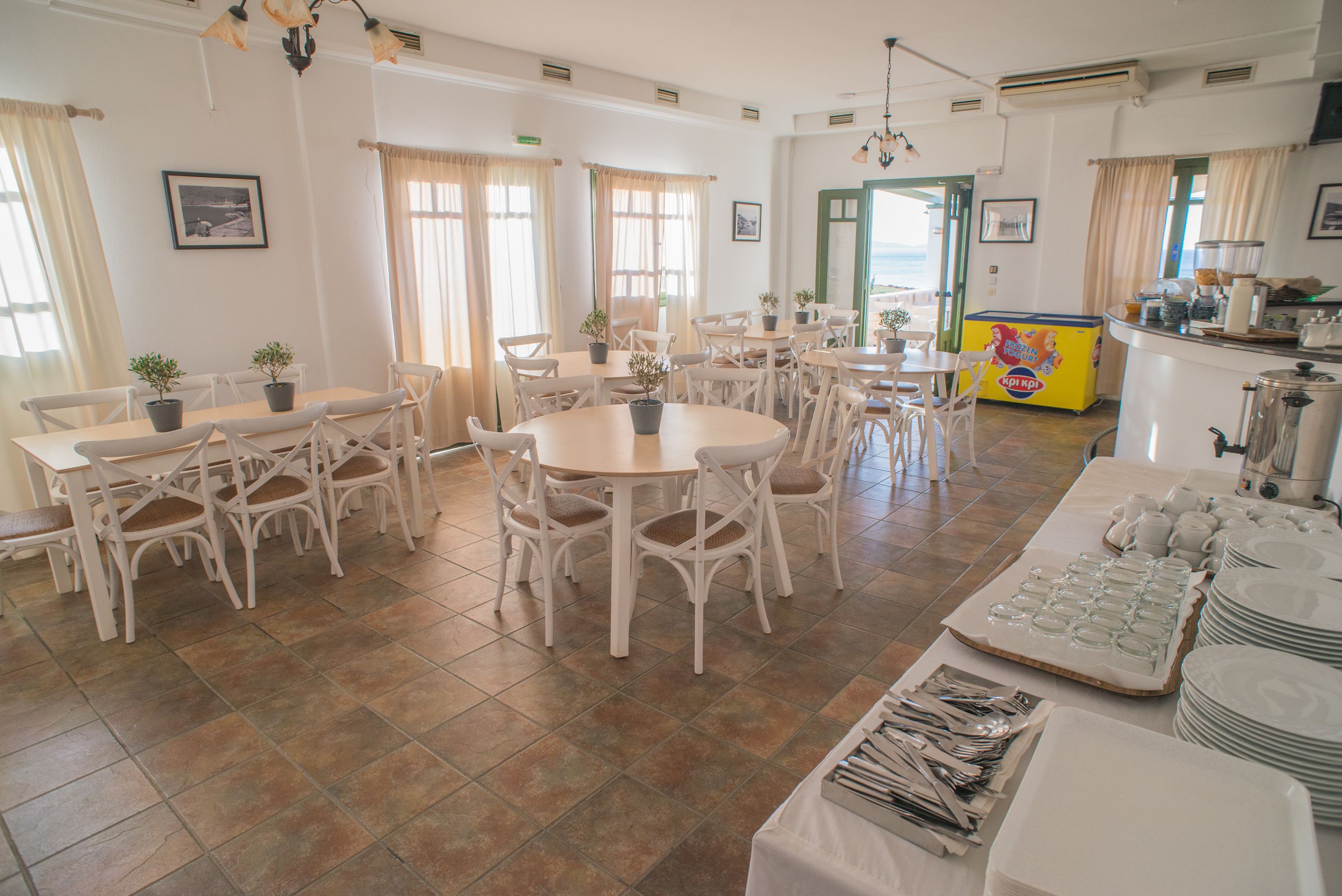 A dining area with multiple tables and chairs, potted plants, and a buffet setup.