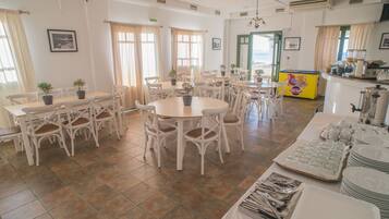 A dining area with multiple tables and chairs, potted plants, and a buffet setup.