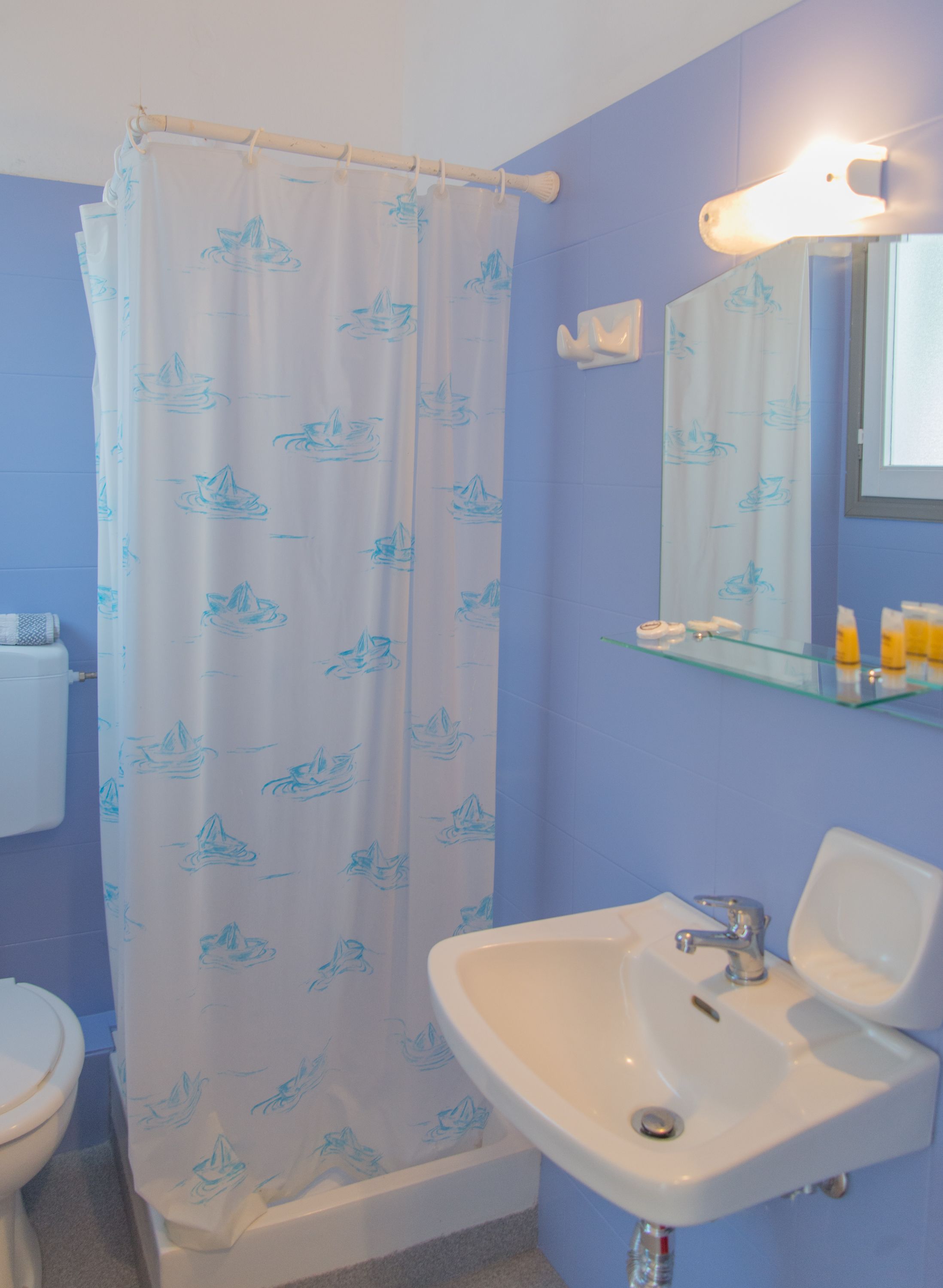 Un baño con cortina de ducha de temática náutica, un lavabo blanco y un espejo encima.