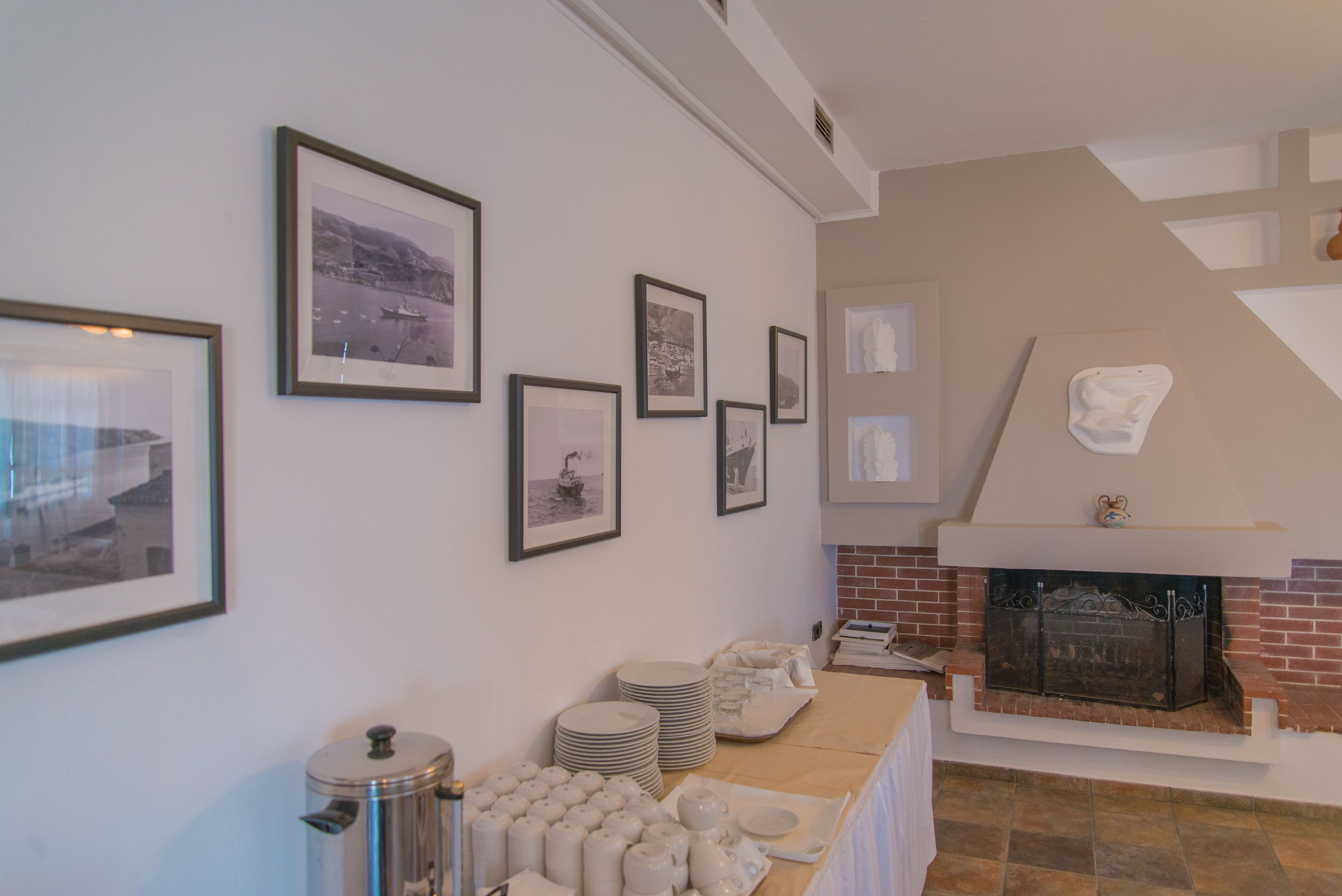 A room with a fireplace, framed pictures on the wall, and a buffet table with plates and cups.