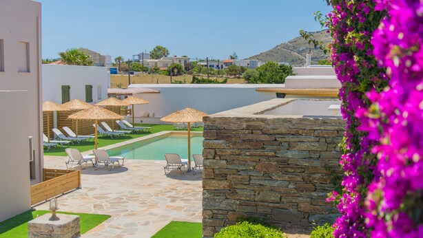 Zona de piscina con sillas de descanso y sombrillas, rodeada de muros de piedra y vegetación.