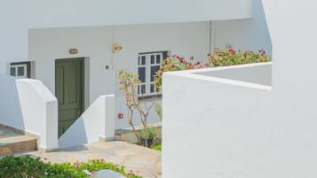 A white building with green shutters and a small garden area with flowers and a large rock.