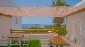 Una terraza con mesa y sillas de madera, un banco y vistas al mar y edificios.