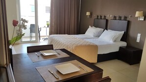 Hotellihuone, jossa on sänky, yöpöydät, työpöytä tuolilla sekä ruokapöytä, joka on katettu kahdelle henkilölle.